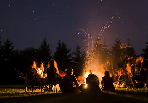 A group of visitors sit around a fire pit amongst the christmas trees of Dull's Tree Farm.